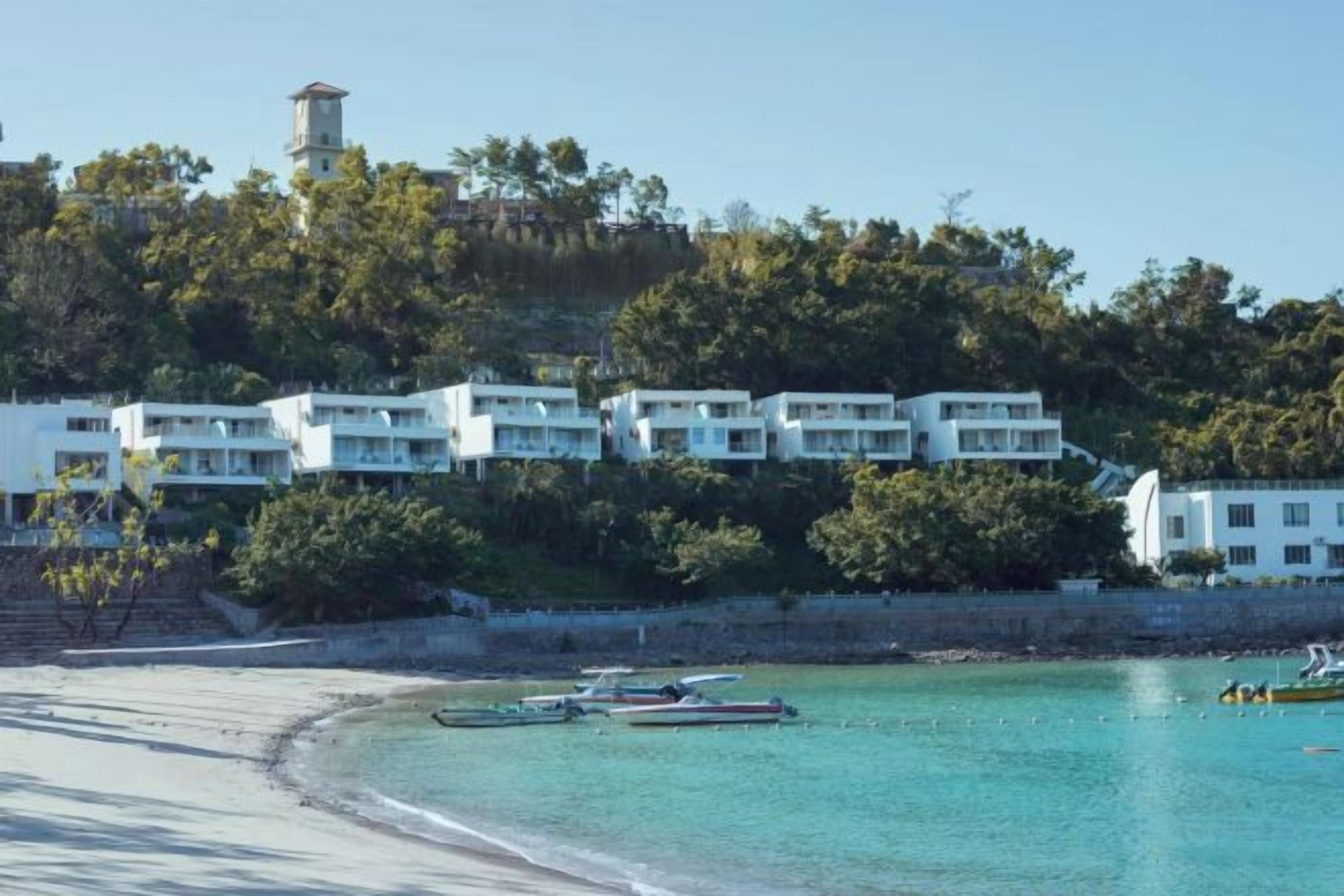 Um hotel costeiro com vários edifícios brancos, uma praia e barcos na água.
