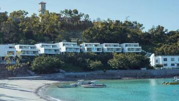 A coastal hotel with multiple white buildings, a beach, and boats in the water.