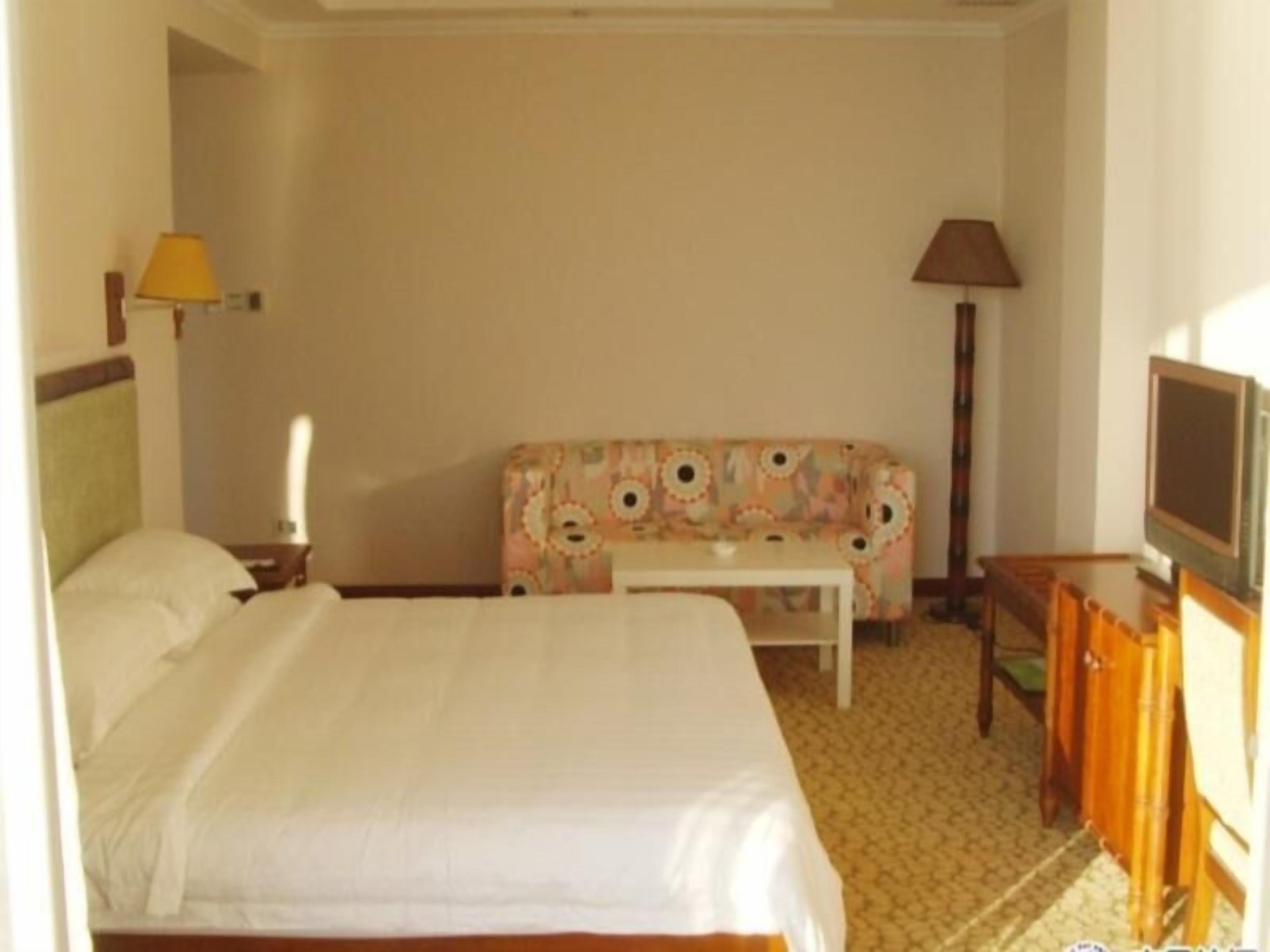 Una habitación de hotel con cama, sofá, televisión y lámpara.