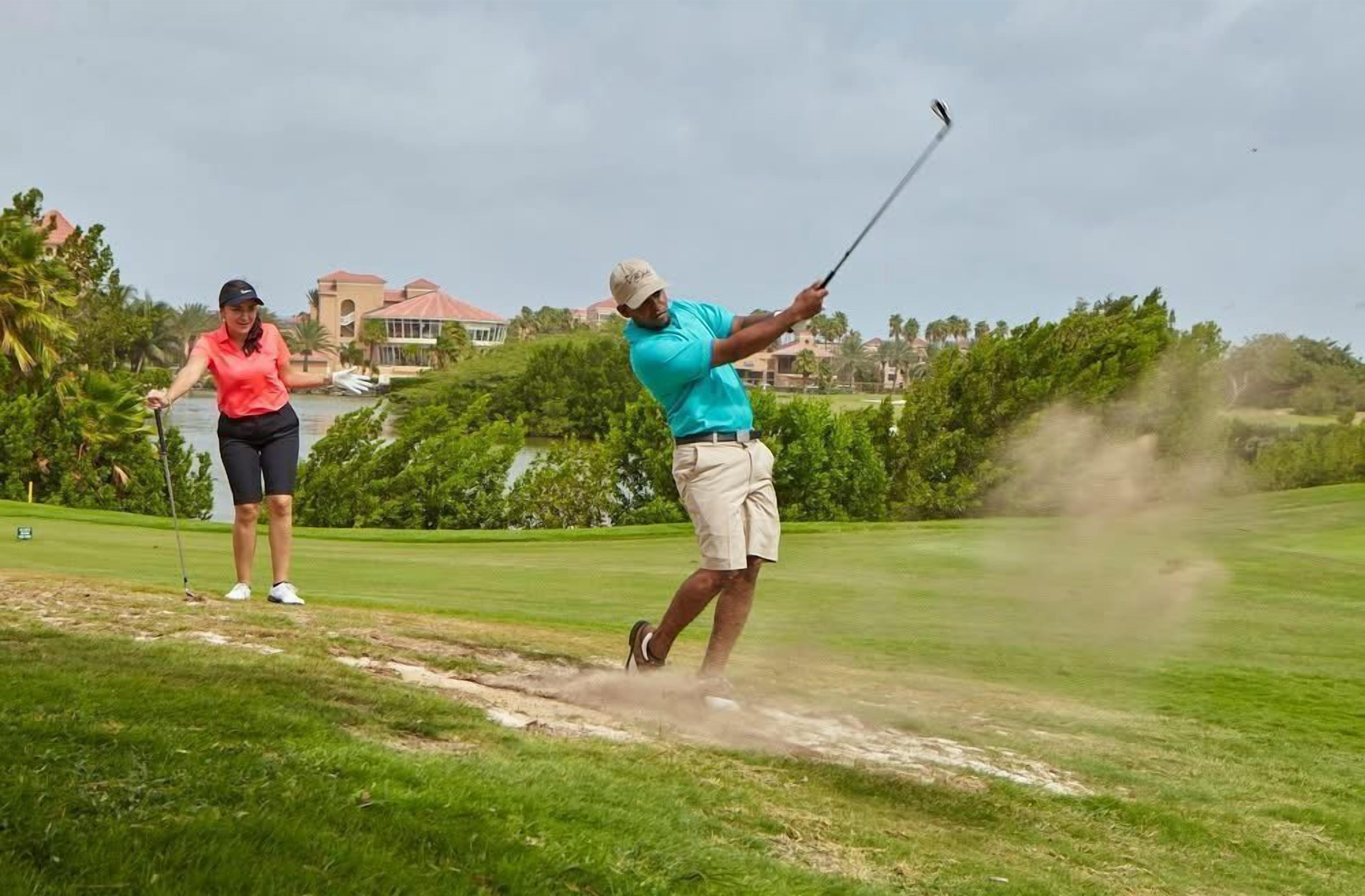 A golf course with a sand bunker and a building in the background.