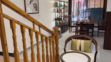 Una escalera de madera conduce a un comedor con una mesa redonda y sillas, una estantería y vistas a la calle.