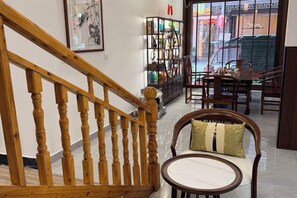 Un escalier en bois mène à une salle à manger où se trouvent une table ronde et des chaises, une bibliothèque et une vue sur la rue.