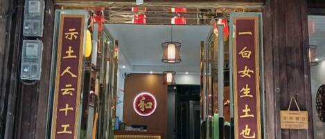 Entrada de um hotel com estilo arquitetônico tradicional chinês, apresentando uma placa de entrada vermelha e dourada, um balcão de recepção e um pendão.