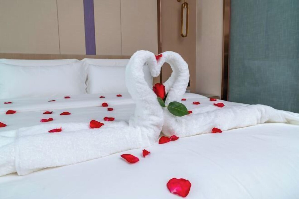 A neatly made bed with rose petals and a swan-shaped towel arrangement.