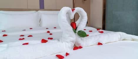 A neatly made bed with rose petals and a swan-shaped towel arrangement.