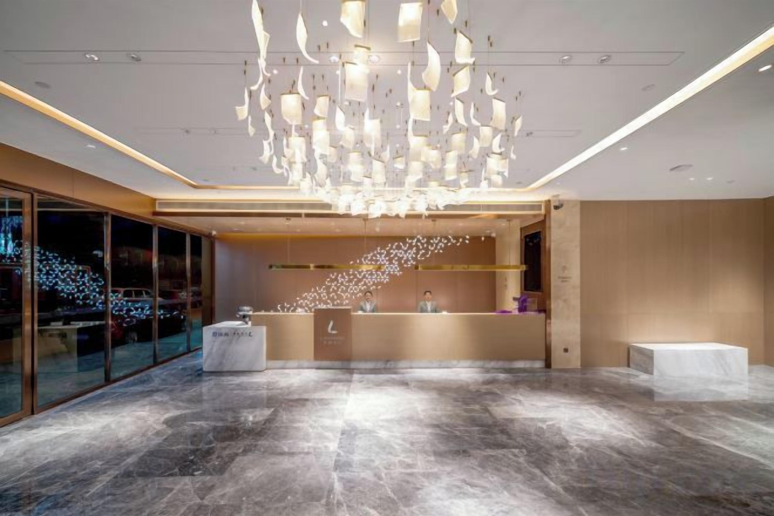 A modern hotel lobby with a marble floor, a reception desk, and a unique ceiling light fixture.