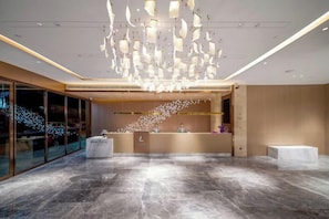 Un moderno vestíbulo de hotel con piso de mármol, una recepción y una lámpara de techo original.