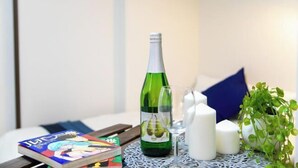 Una botella de champán, una copa, velas, un libro y una planta pequeña sobre una mesa.