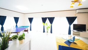 Una sala de estar moderna con una mesa de ping pong, un televisor de pantalla plana y una pared de acento amarilla.