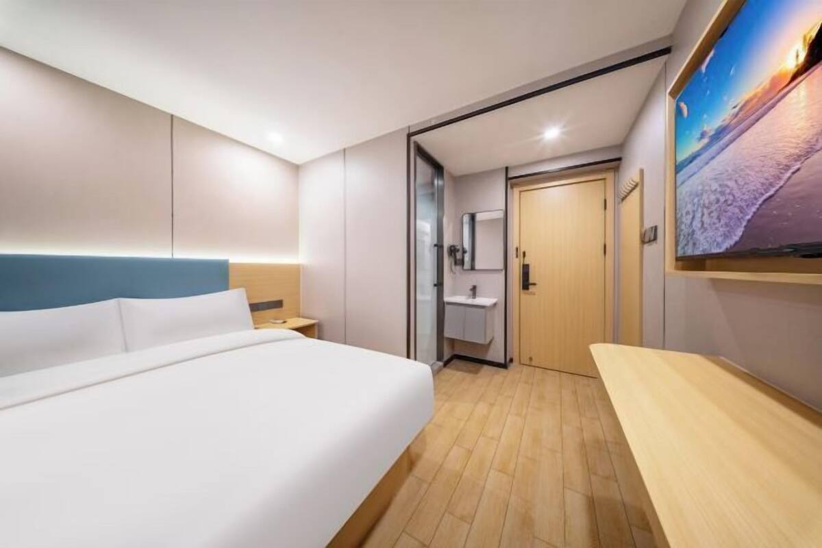 A hotel room with a bed, a bedside table, a nightstand, a bathroom with a sink, and a large window.