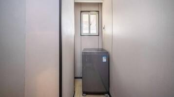 Un pasillo estrecho con una puerta al final, una ventana y un refrigerador pequeño.