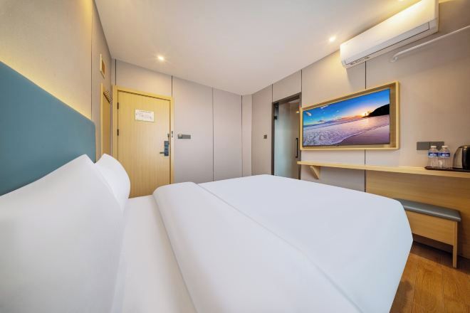 Quarto de hotel com cama, escrivaninha, cadeira, televisão e porta.