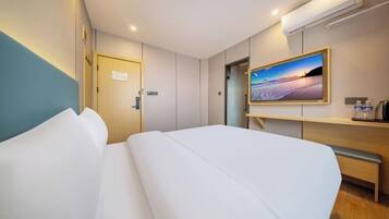 Quarto de hotel com cama, escrivaninha, cadeira, televisão e porta.