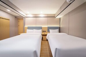 A hotel room with two beds, a wooden door, a nightstand, and a wall-mounted light fixture. - Shanghai Wankai Collection Hotel (Shanghai)
