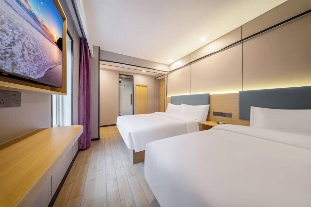 A hotel room with two beds, a TV, a wooden bench, and a view of the sea.