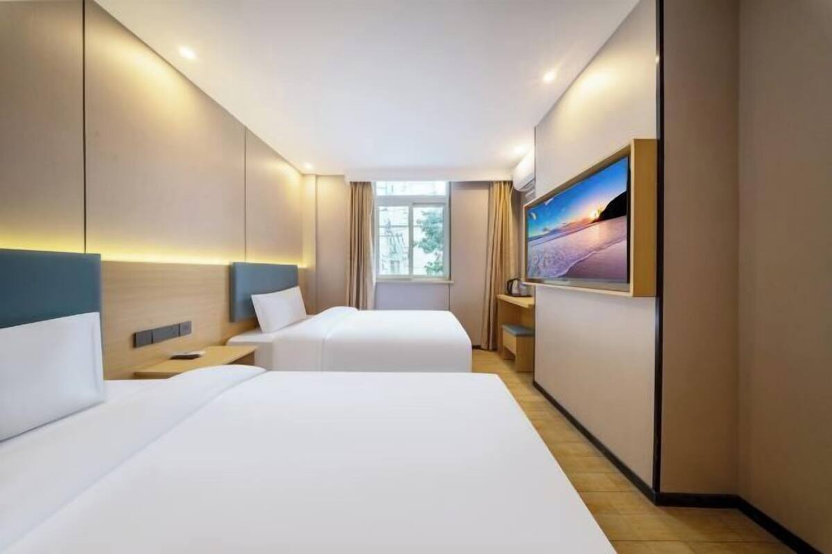 A hotel room with two beds, a TV, a window, and a view of the outdoors.