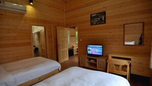 Una habitación tipo cabaña de madera con dos camas, un televisor, un escritorio y un espejo.