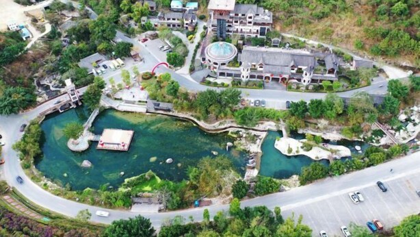 Vista aérea de un resort con un estanque central, conectado por senderos, rodeado de exuberante vegetación y edificios de arquitectura tradicional.