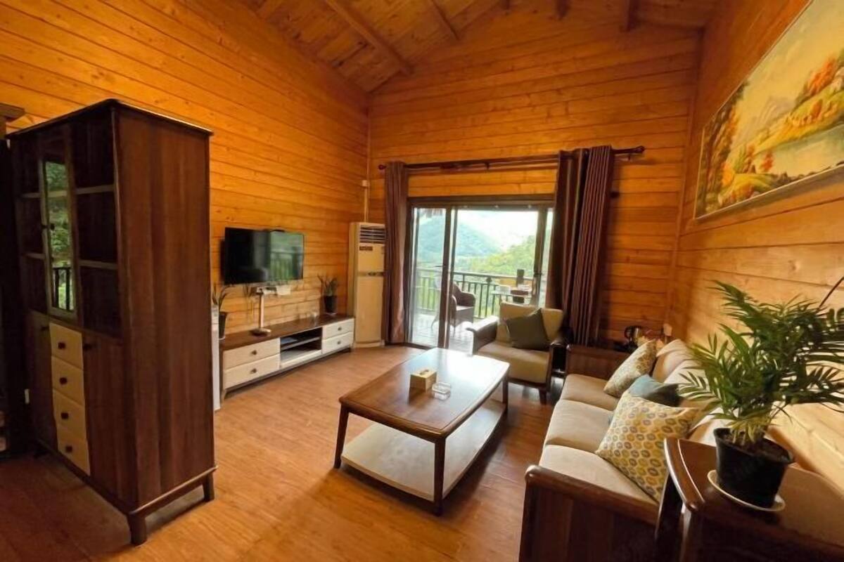 Una habitación con paneles de madera, un sofá, una mesa de centro, televisión y un balcón con vistas.