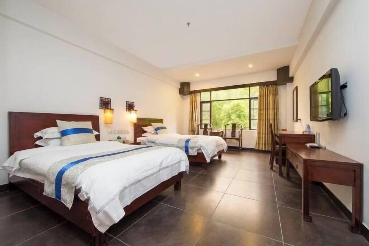Habitación de hotel con dos camas, un escritorio, una silla, un televisor y una ventana con cortinas.