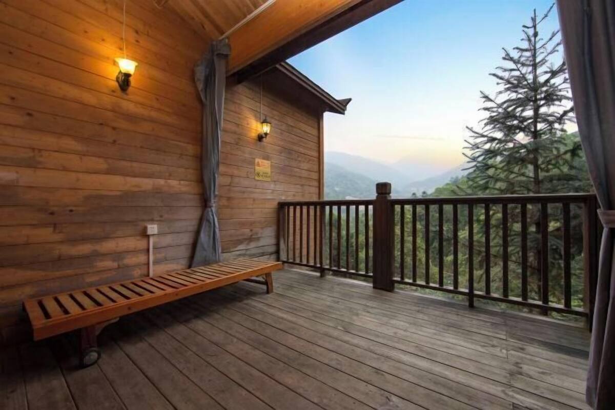 Terraza de madera con un banco, dos luces fijadas a la pared y vistas de una cordillera.