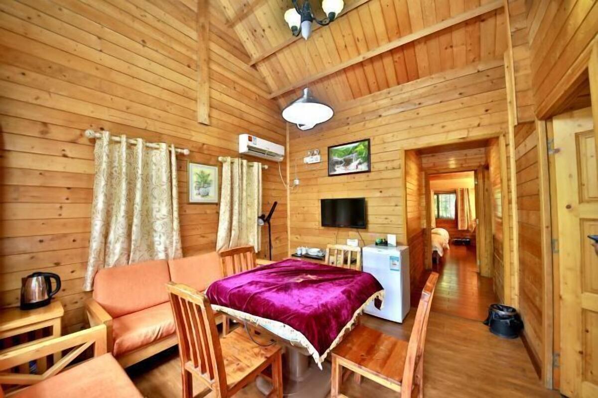 Interior de una cabaña de madera con sofá, mesa de comedor, sillas, televisor y equipo de aire acondicionado.