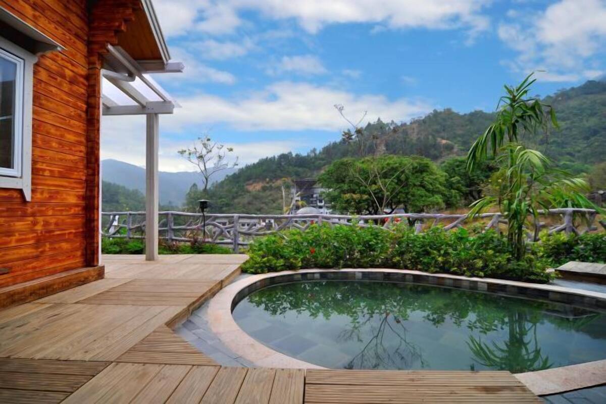 Una casa de madera con piscina, rodeada de exuberante vegetación y montañas al fondo.