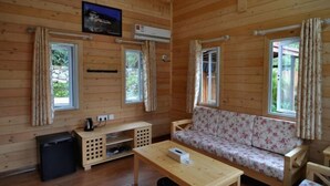 Interior de una cabaña de madera con sofá, una mesita, televisor y refrigerador.