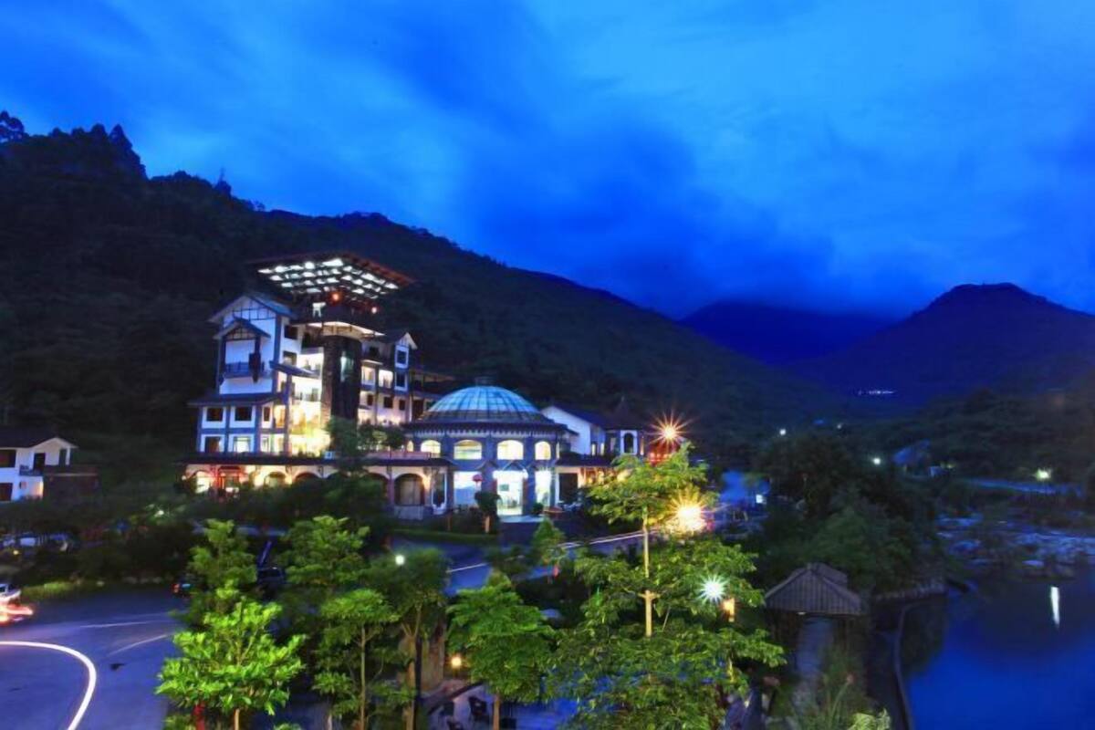 Un gran hotel de varios pisos con una cúpula destacada y múltiples balcones, rodeado de vegetación exuberante y un telón de fondo montañoso.