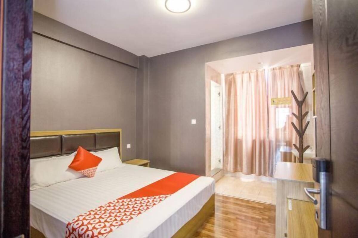 A hotel room with a bed, a nightstand, a wooden floor, and a door leading to a corridor.