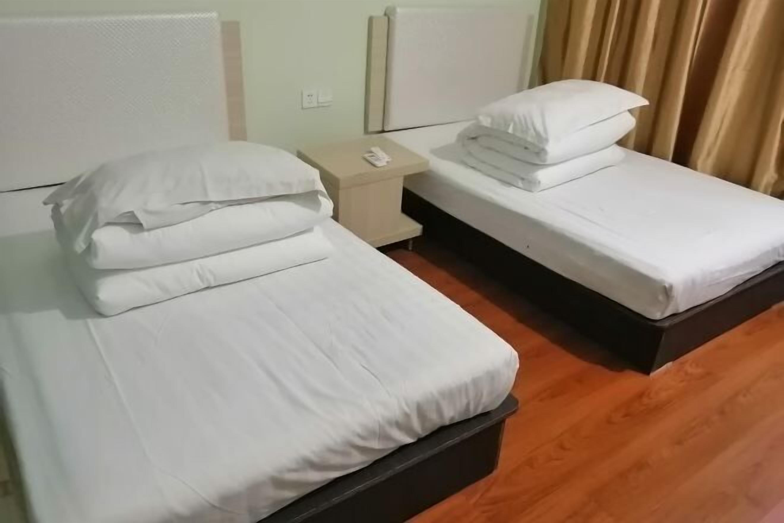 A hotel room with two beds, each with white bedding and pillows, a small bedside table, and a nightstand.