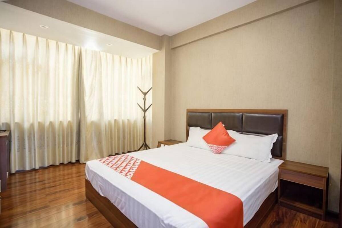 A hotel room with a large bed, a bedside table, a lamp, and a window with curtains.