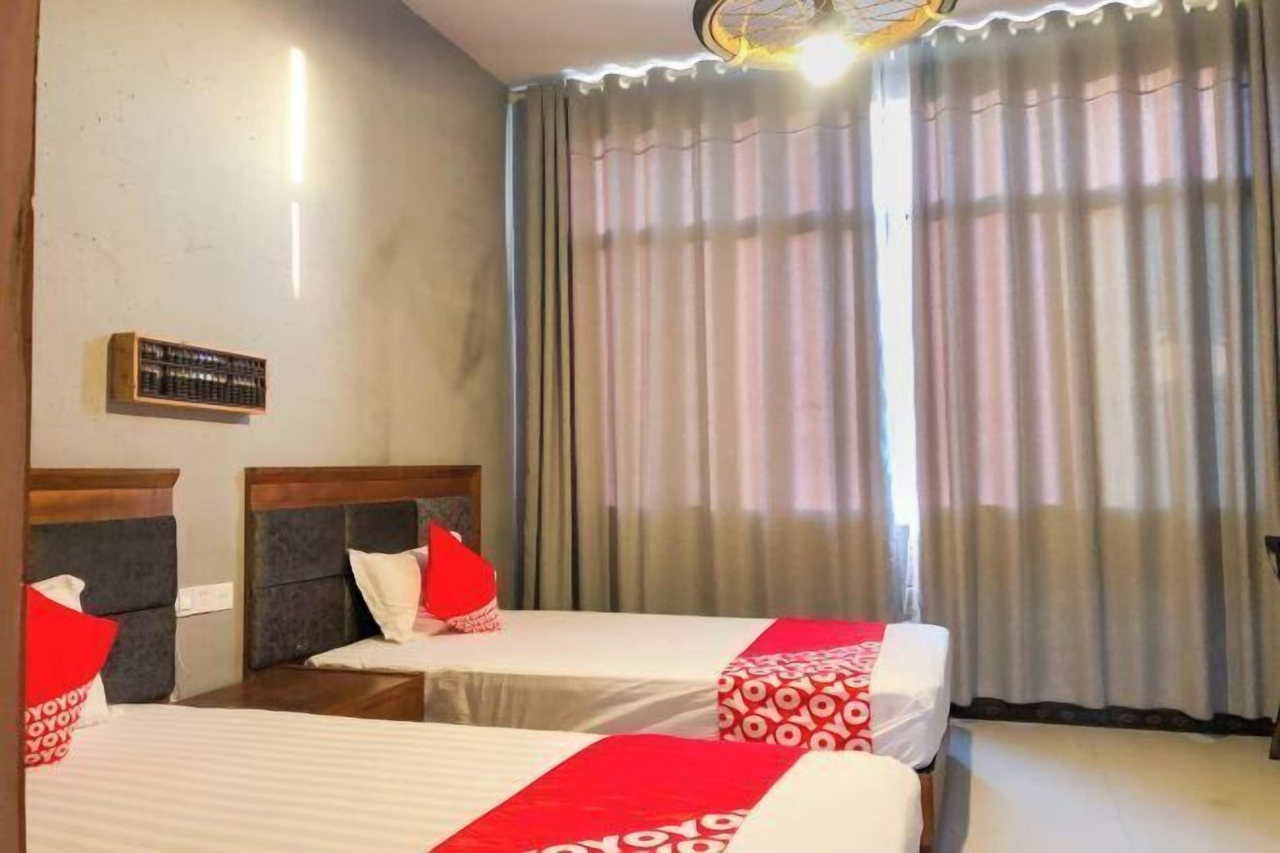 A hotel room with two beds, each with a red and white bedspread, and a large window with curtains.