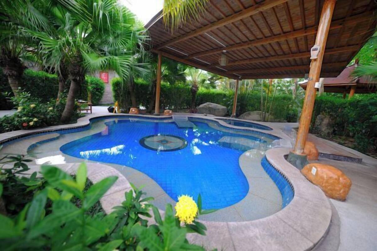 A swimming pool with a curved design, surrounded by tropical plants and a wooden pergola.