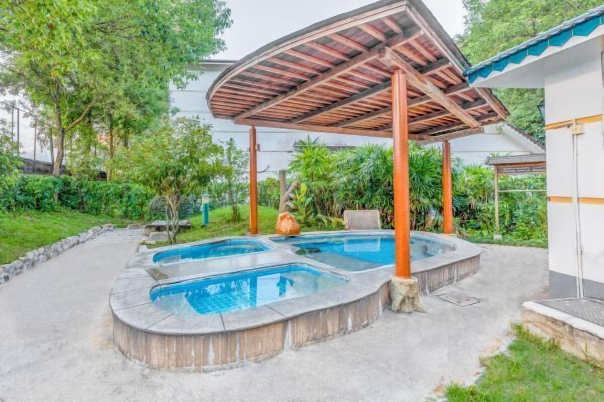 A pool area with a covered structure, surrounded by greenery.