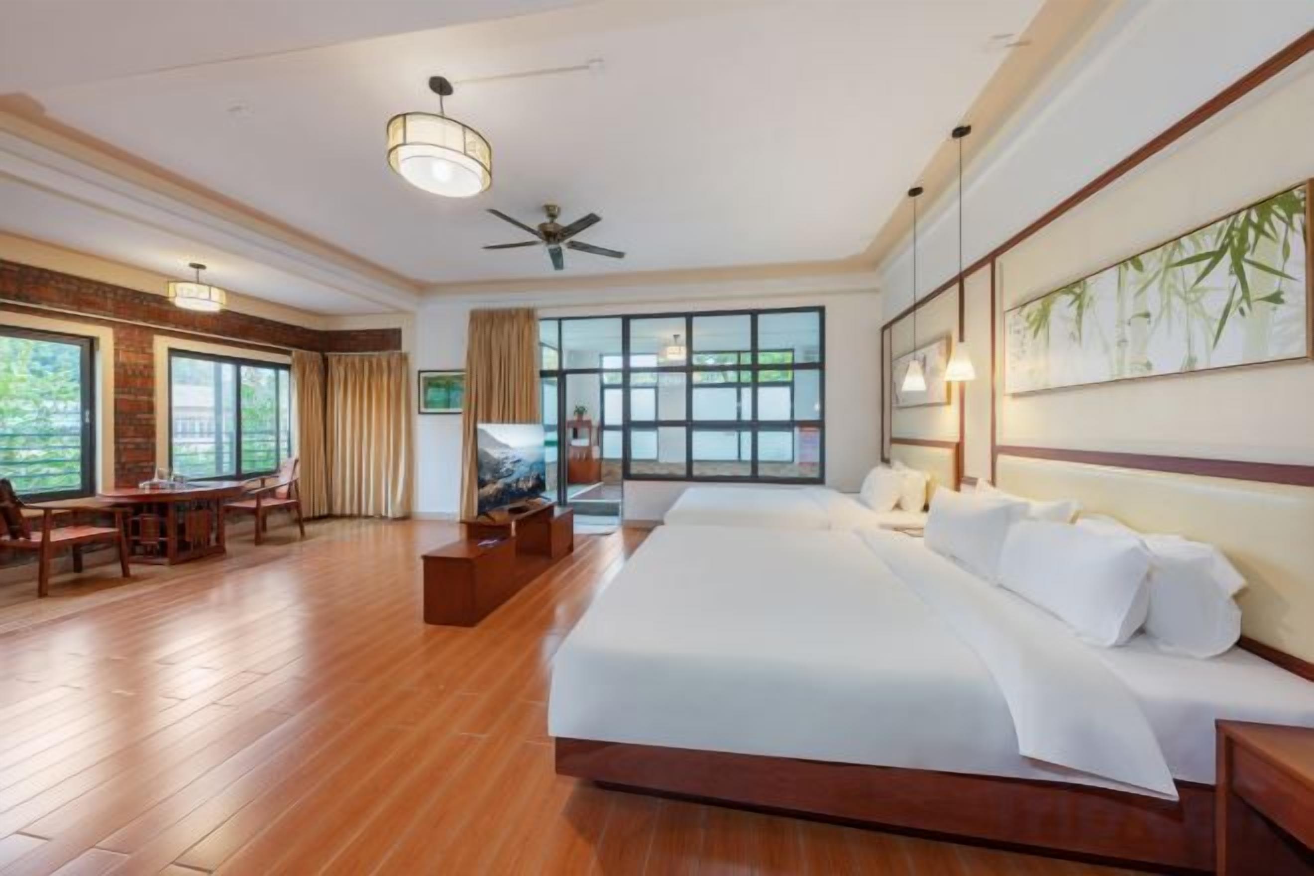 A hotel room with a large bed, a desk, a chair, a television, and a ceiling fan.