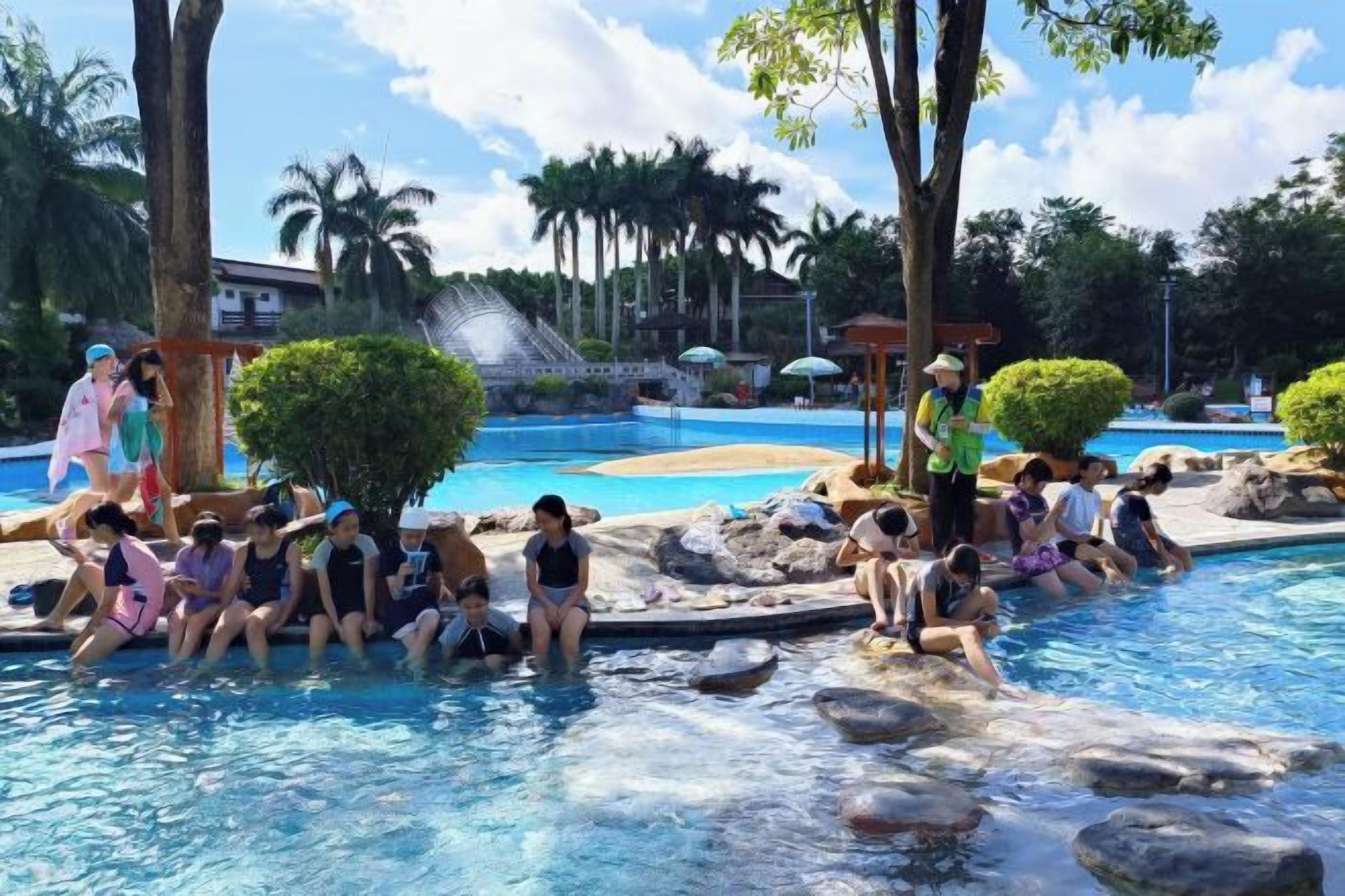 A swimming pool area with people sitting and standing around.