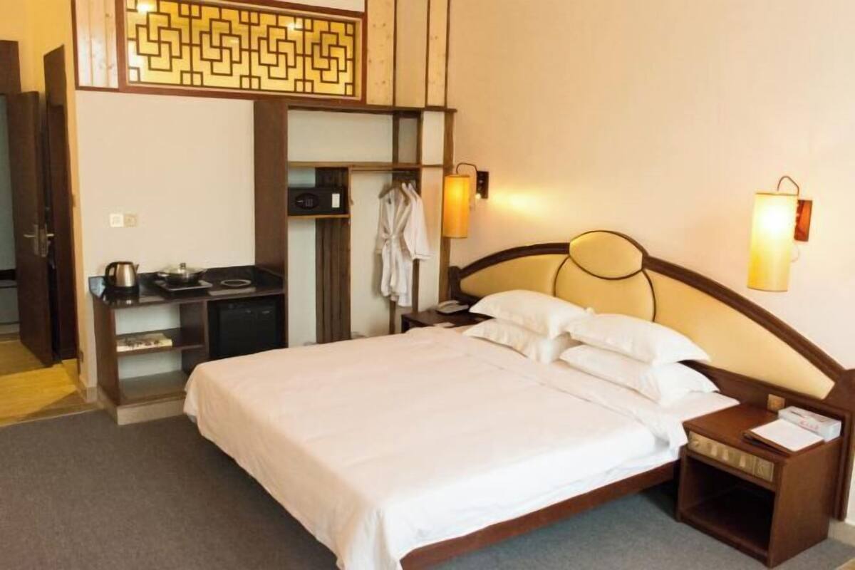 A hotel room with a bed, bedside table, lamp, and a wardrobe with a mirror.