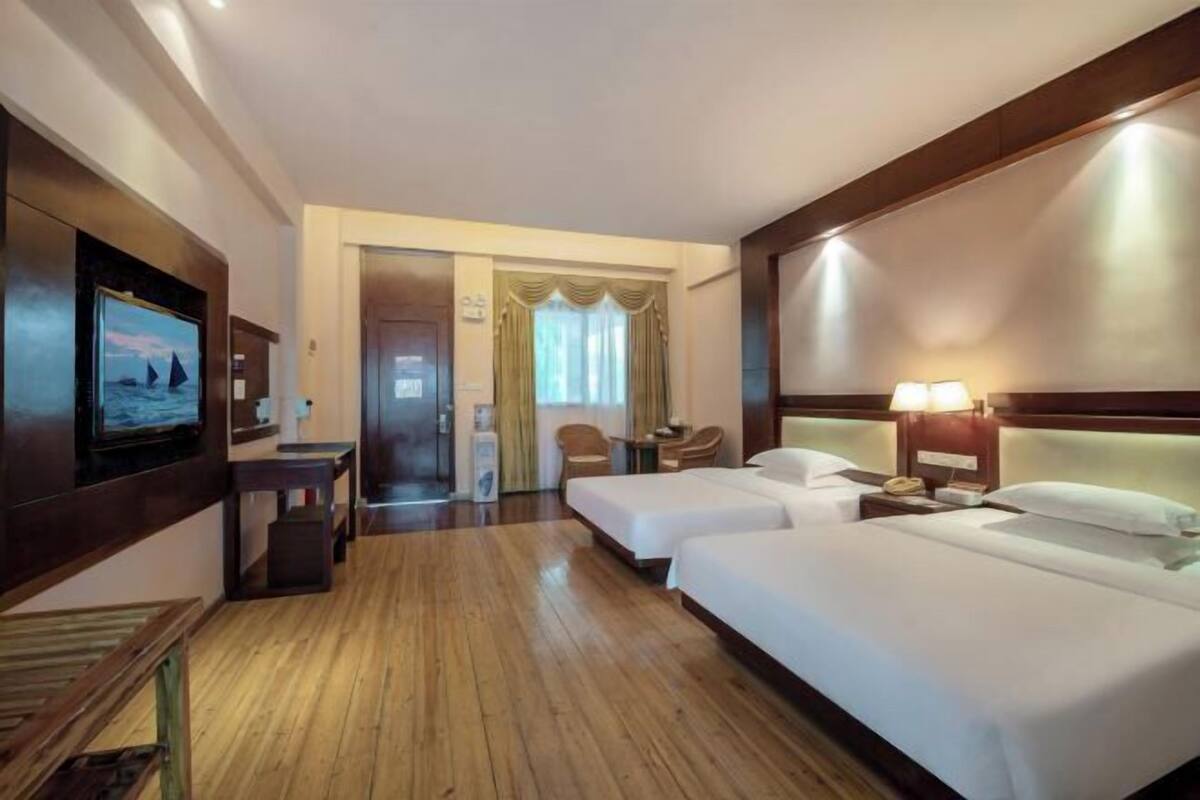 A hotel room with two beds, a television, a desk, and a chair.