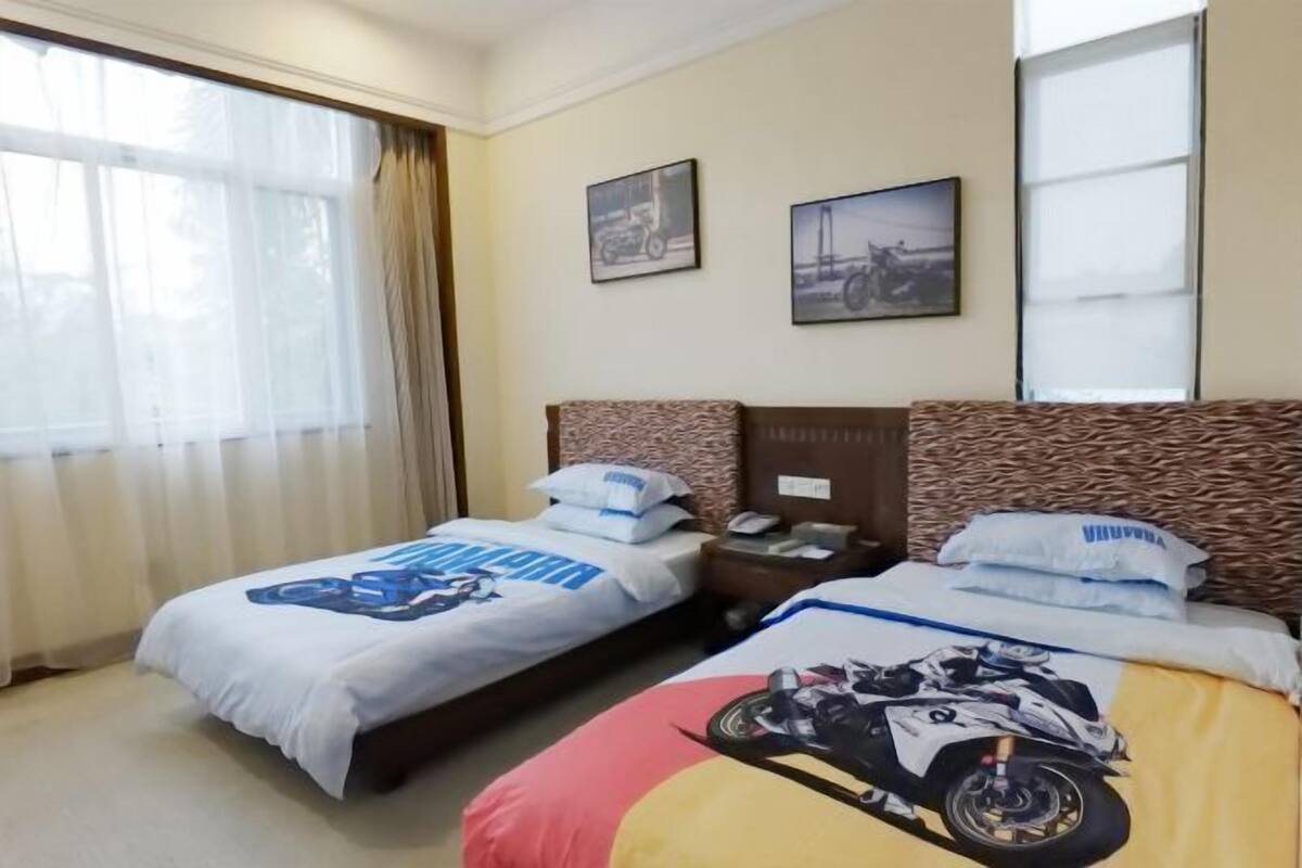 A hotel room with two beds, a large window with curtains, and two framed pictures on the wall.