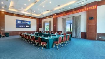 Un salón de conferencias con una larga mesa, sillas, una pantalla de proyector y un amplio ventanal.
