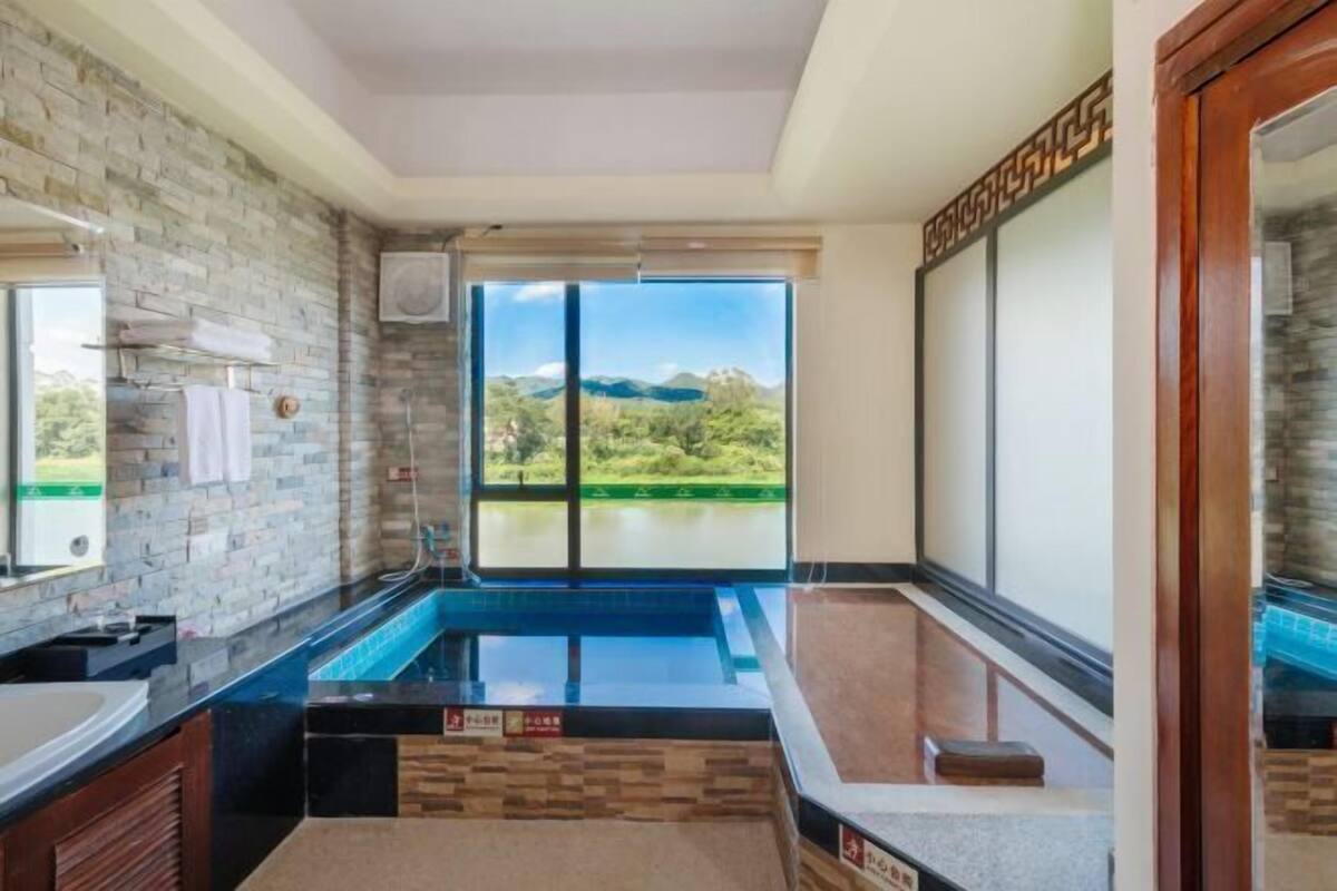 A modern bathroom with a large window, a built-in bathtub, and a stone wall.