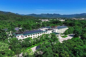 A large building with multiple floors, surrounded by lush greenery and mountains in the background. - Enping Jinjiang Hotspring Hotel (Enping)