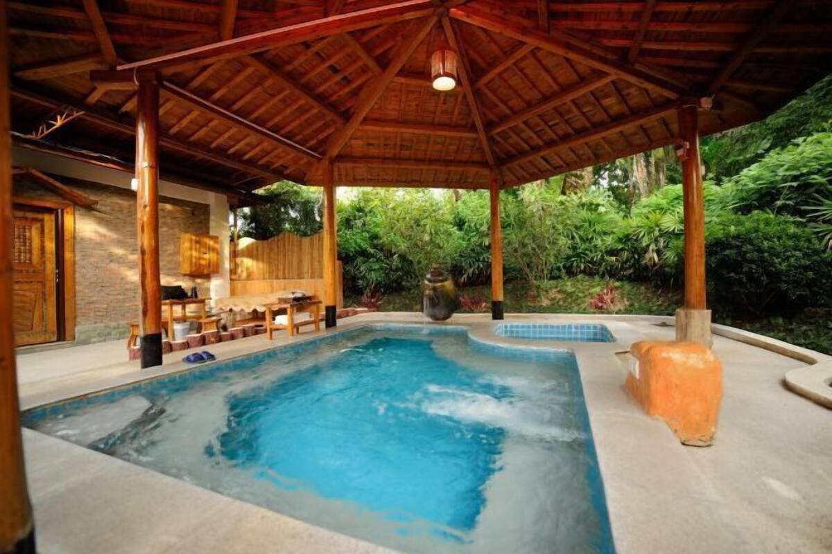 A pool area with a wooden gazebo, stone walls, and lush greenery.