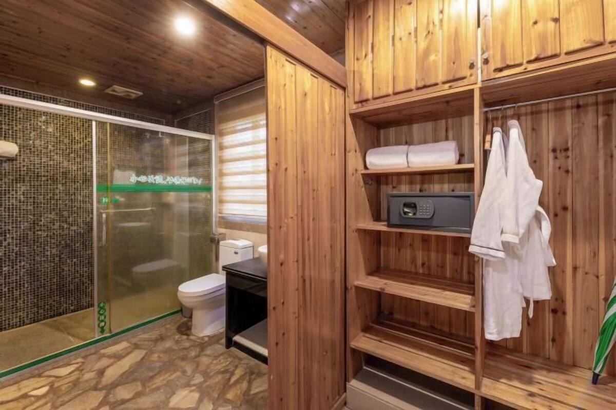 A wooden interior with a glass-enclosed shower, a toilet, and a shelf with towels.