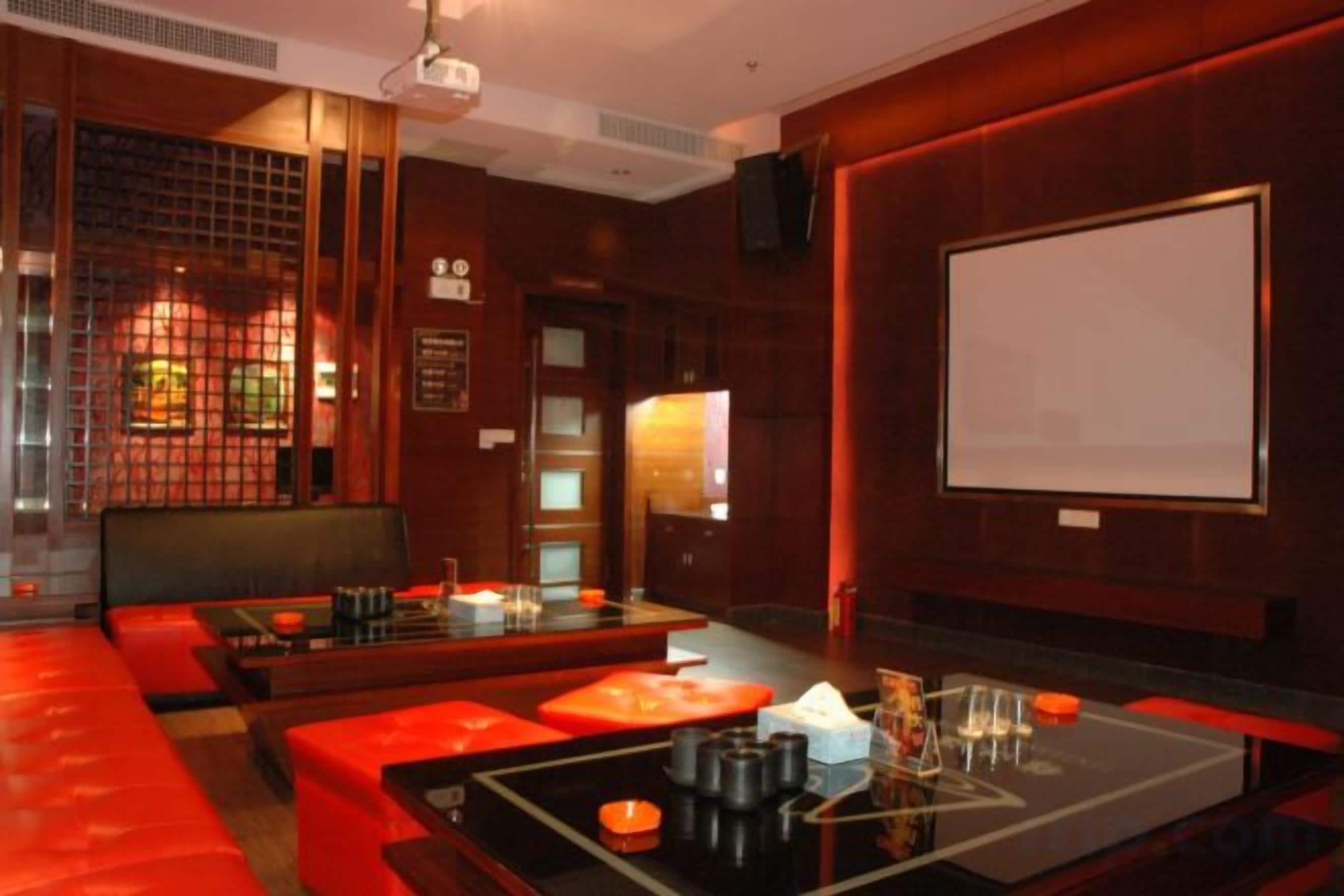 Una sala tenuemente iluminada con una pantalla de proyector, asientos rojos y una mesa con diversos objetos.