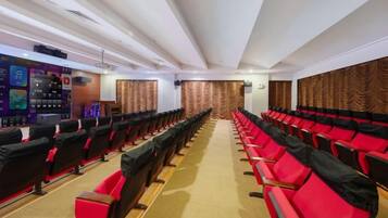 A conference room with rows of black and red chairs, a stage with a podium, and a carpeted floor.