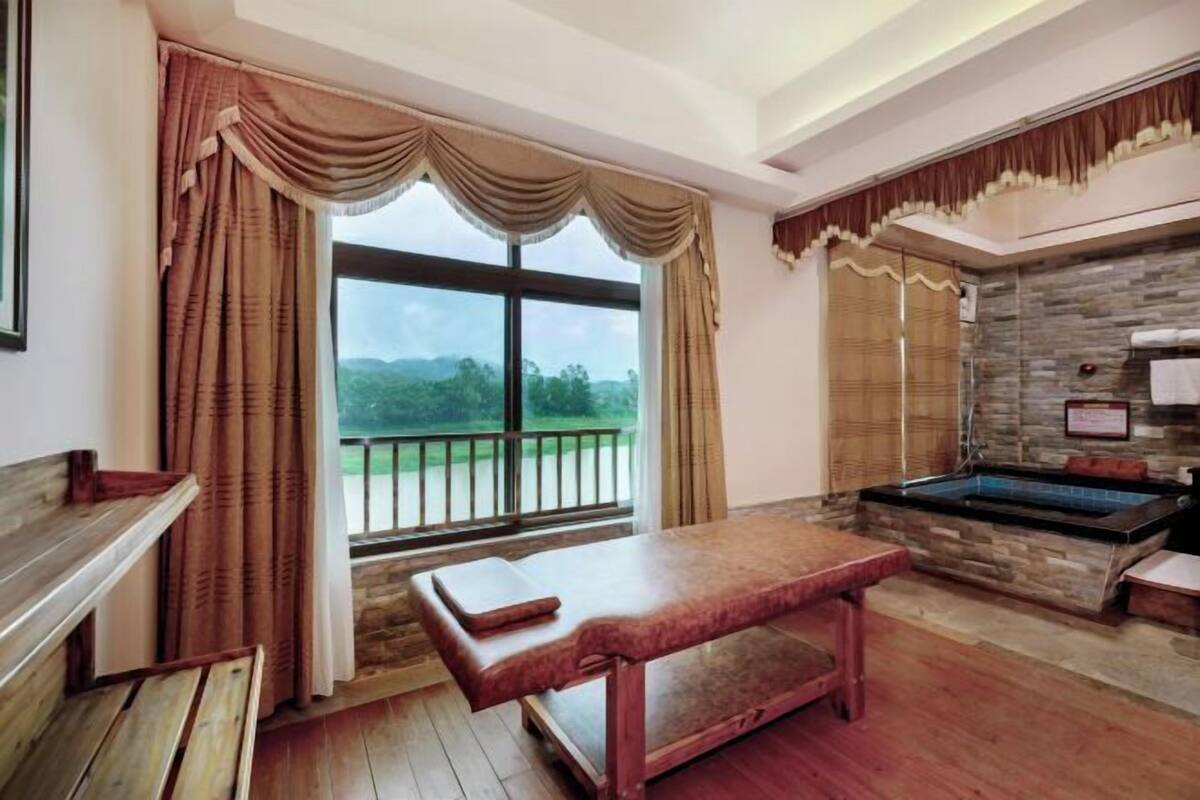 A room with a wooden bench, a stone wall, and a view of greenery outside.