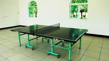 Una mesa de ping pong con ruedas en una habitación con suelo de baldosas y dos ventanas arqueadas.