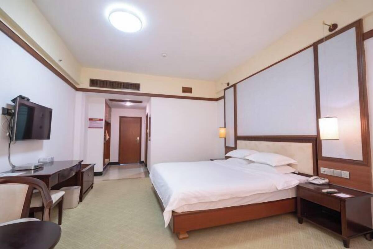 A hotel room with a bed, bedside table, lamp, desk, chair, and a television.